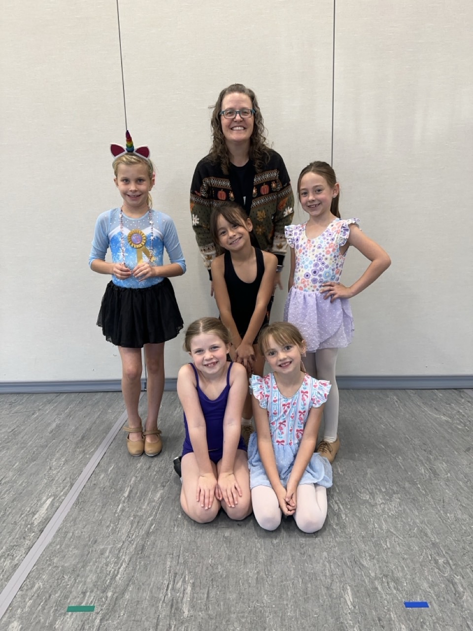 A teacher and five young dancers smiling together in the dance studio.