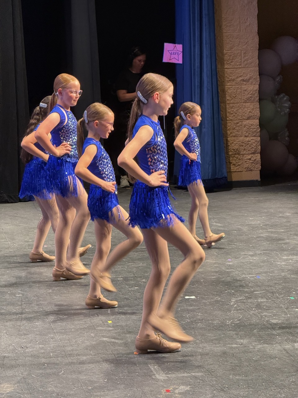 Young dancers performing on stage in blue sequined and fringed recital costumes.