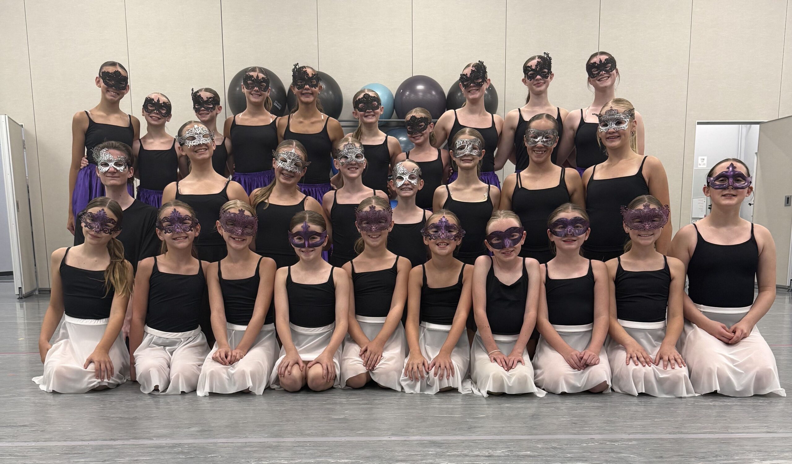 E&E Dance Company dancers posing together in the studio wearing masquerade masks, black tops, and white or purple skirts.