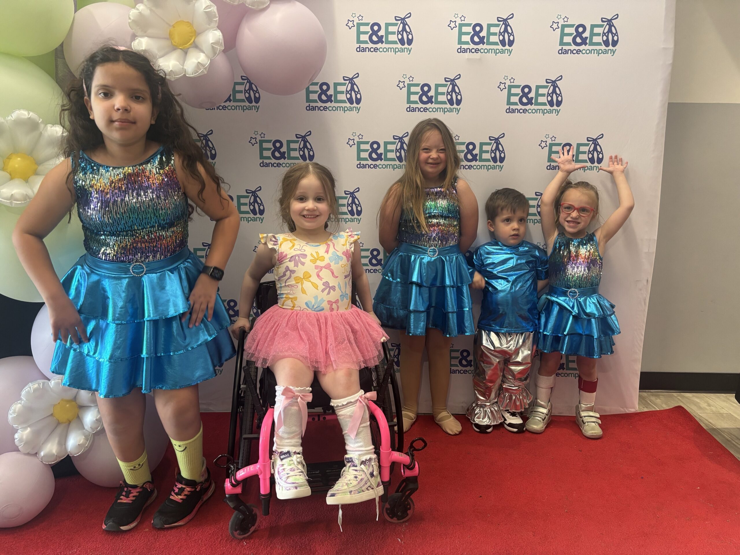 Dancspiration dancers in colorful recital outfits posing in front of the E&E Dance Company backdrop.