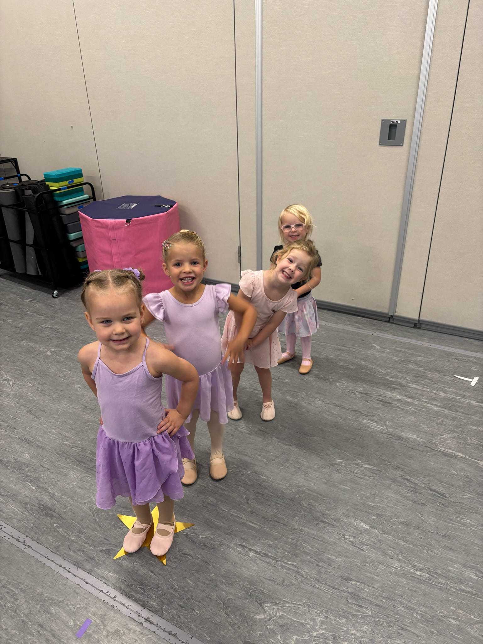 Four smiling young dancers in pastel dancewear standing in a line in the studio.